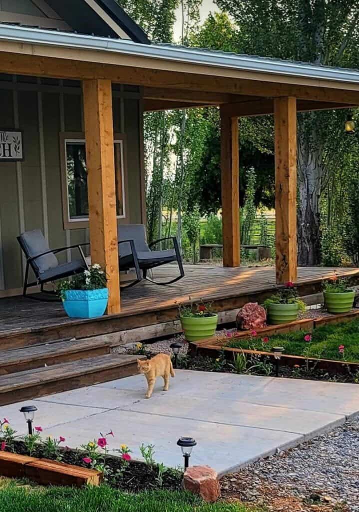 A Utah Homestead front porch with cedar posts. A can walking along the front sidewalk and spring flowers blooming. 