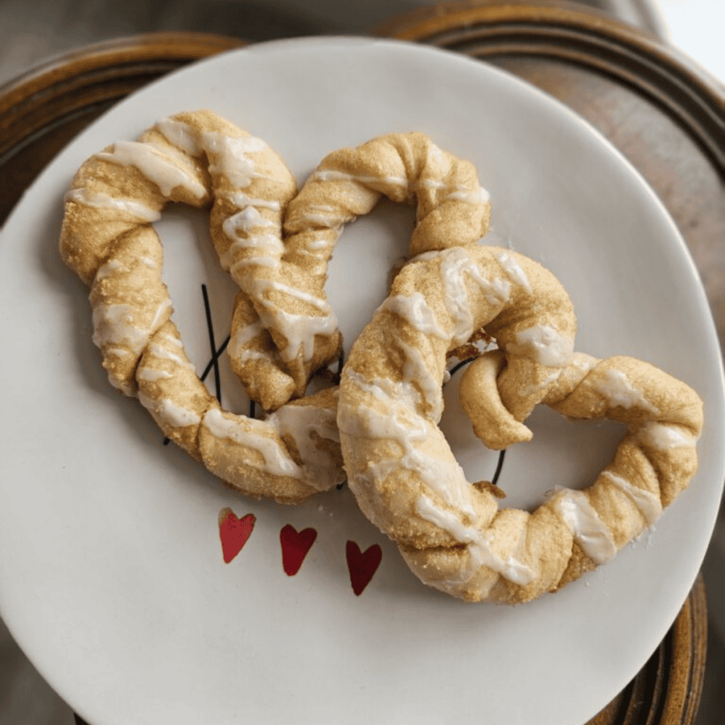 Heart shaped pastry drizzled in frosting on a white plate with red hearts