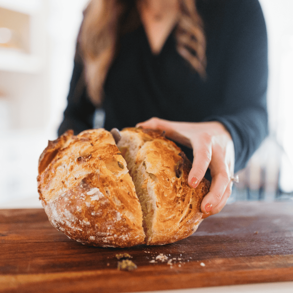 a close up of a woman slicing into a jalapeno cheddar sourdough loaf of bread