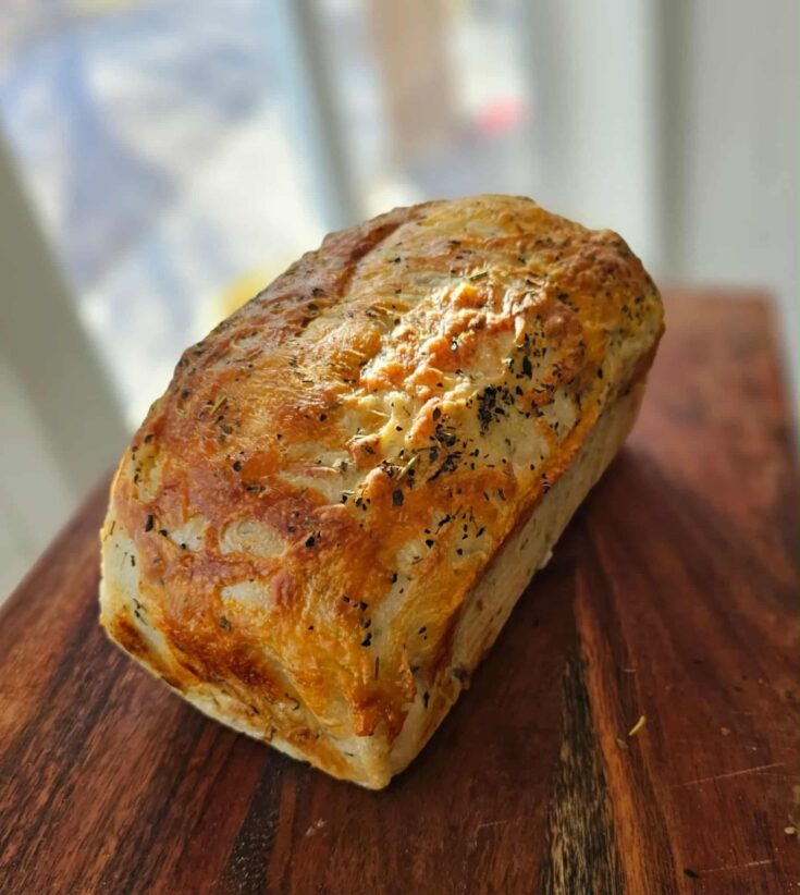 Italian herb and cheese bread whole on a cutting board