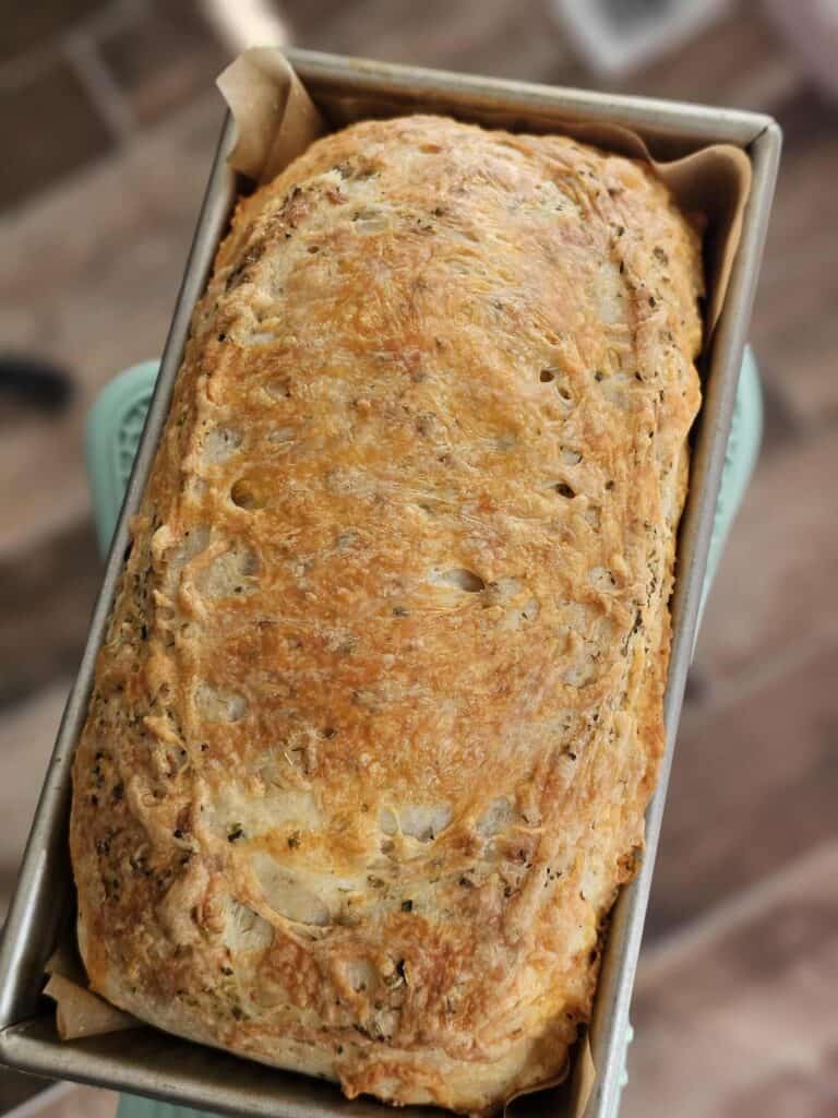 Italian herb and cheese sourdough sandwich bread in a USA loaf pan. Being held by a hand with a oven mitt.